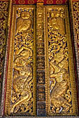 Wat Xieng Thong temple in Luang Prabang, Laos. Detail of a wooden door of the sim with gilded carvings on a red background. 